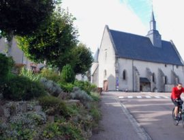 Un cycliste traverse le village, en arrière plan, l’église de Moux